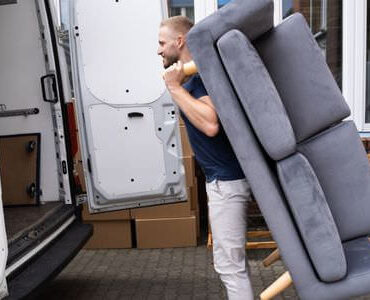 Möbellift Worms Möbellift Worms: Helfer tragen ein graues Sofa aus einem Transporter